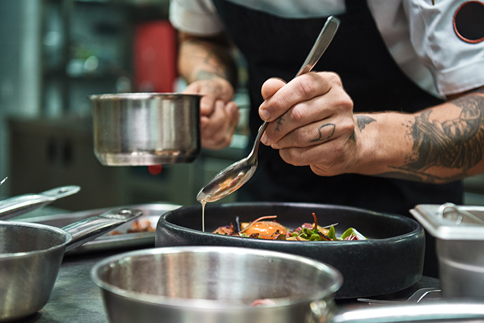 Secret recipe. Close up photo of chef hands with several tattoos adding a sauce to italian pasta Carbonara.